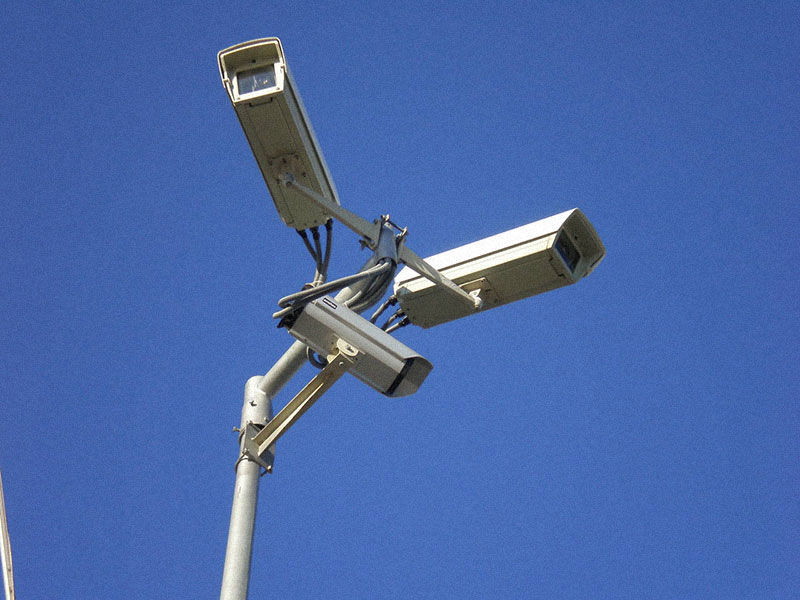 Trois caméras de surveillance montées sur un mât, devant un ciel bleu
