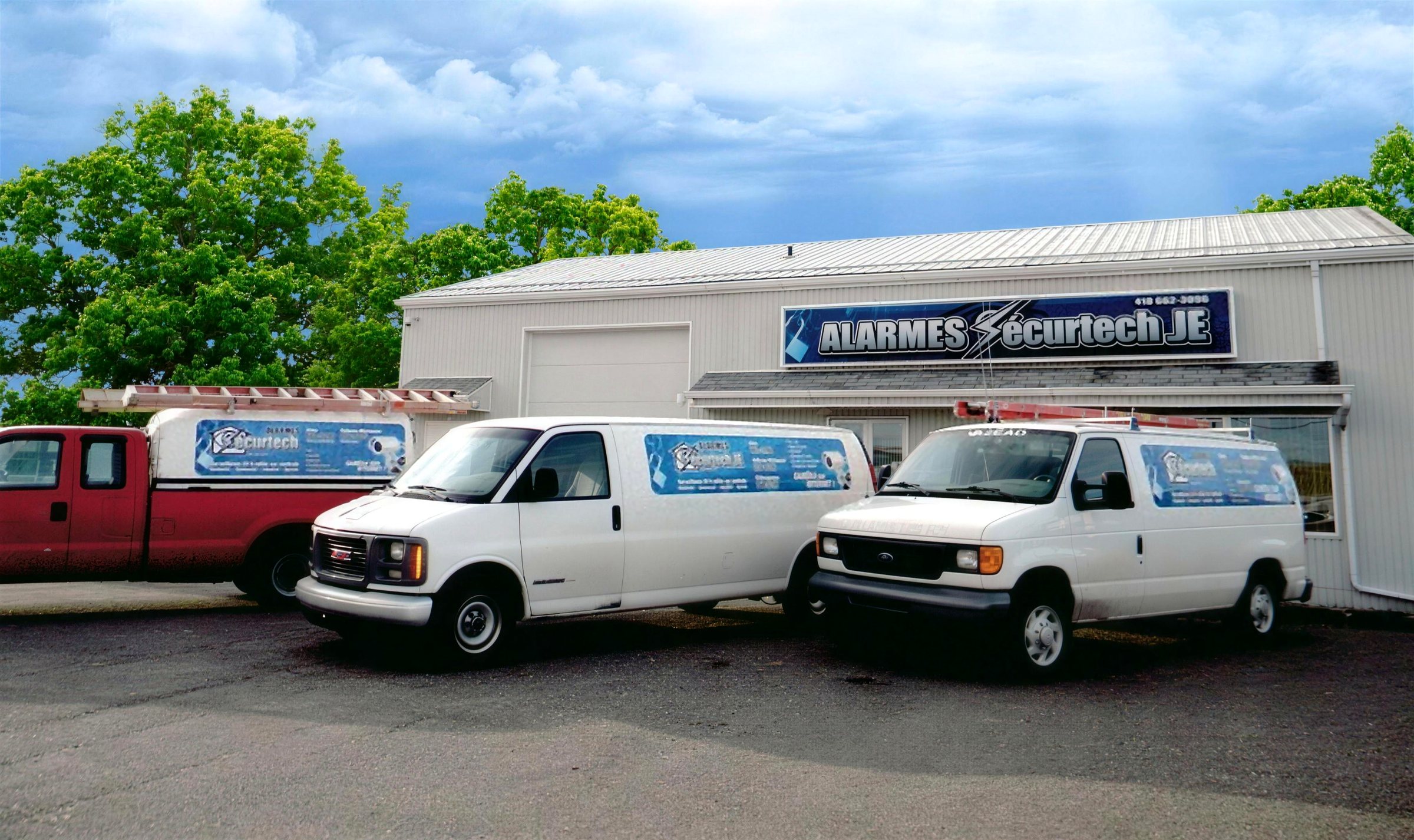 Camionnette et deux fourgonnettes de service aux couleurs d’Alarmes SecurTech JE, stationnées devant les bureaux d’Alma